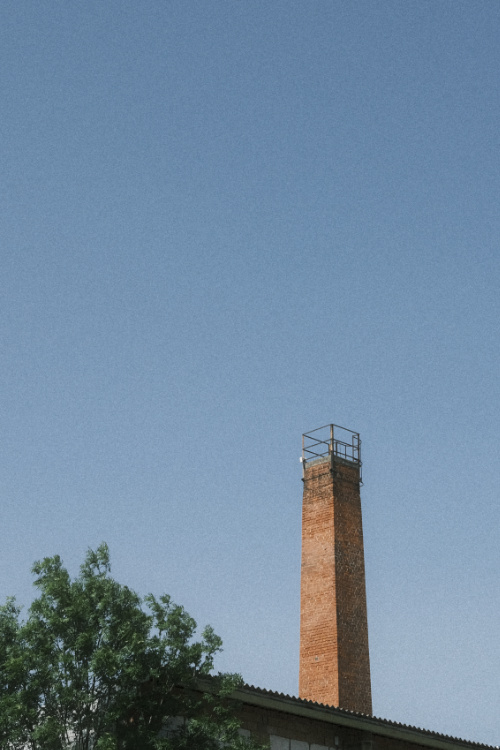 a square smokestack made of red bricks in front of a blue sky without any clouds on a bright, sunny day.